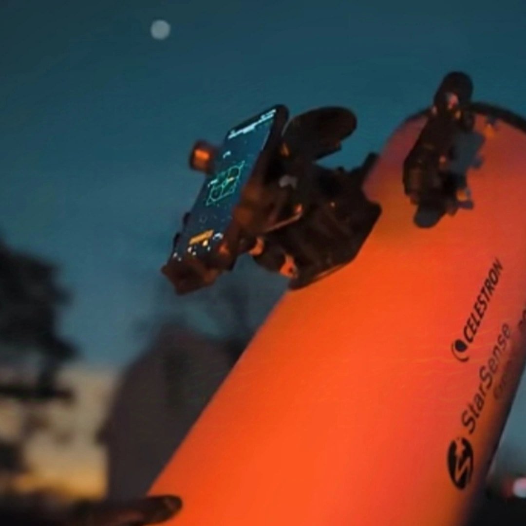 Close detail of the orange Celestron telescope tube against a dark blue sky with the Moon behind it.